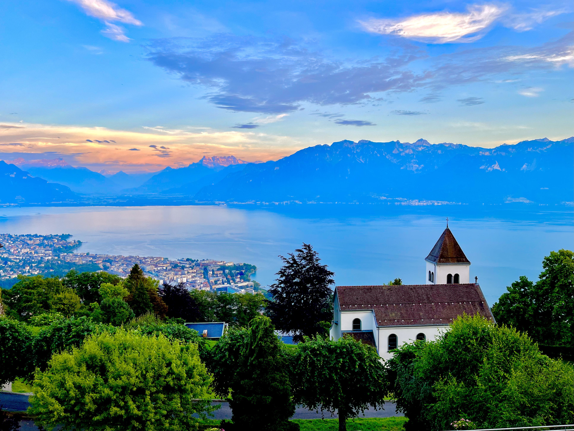 Full-sunshine view of the Alps and Lake Geneva with the roof of a nearby church
